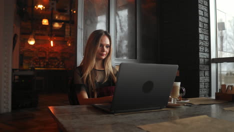 Happy-young-woman-drinking-coffee-and-using-tablet-computer-in-cafe